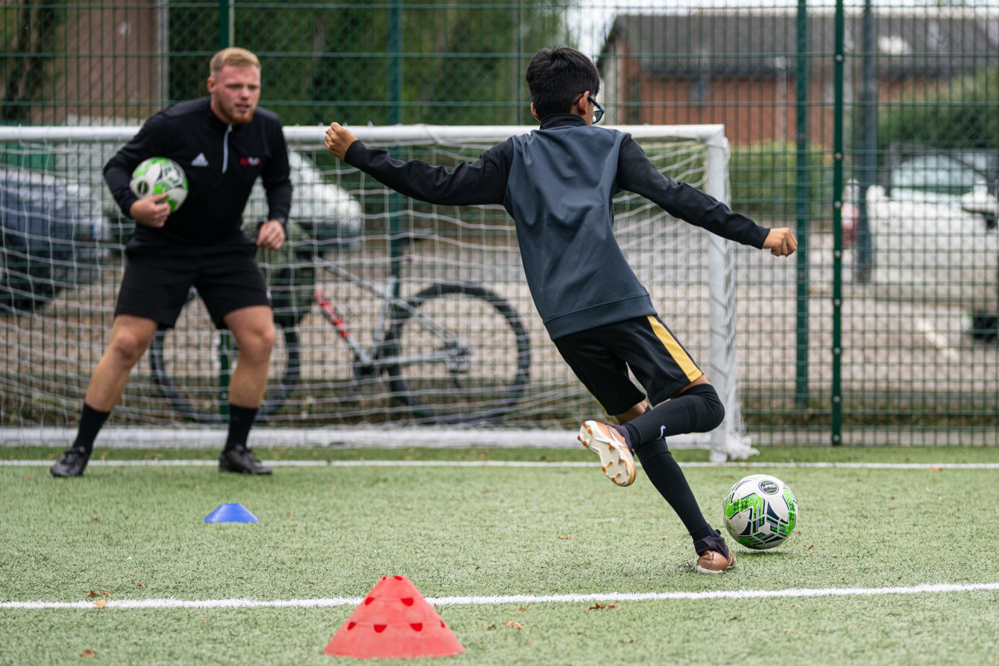 Coach Dan in goal as a young player lines up a shot at a Kick On session